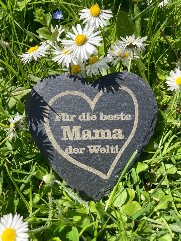Herz aus Stein mit der Aufschrift "Für die beste Mama der Welt" umgeben von Blumen.