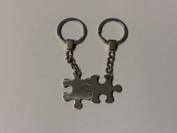 Zwei silberne Schlüsselanhänger in Form von Puzzlestücken, an einer Kette befestigt.