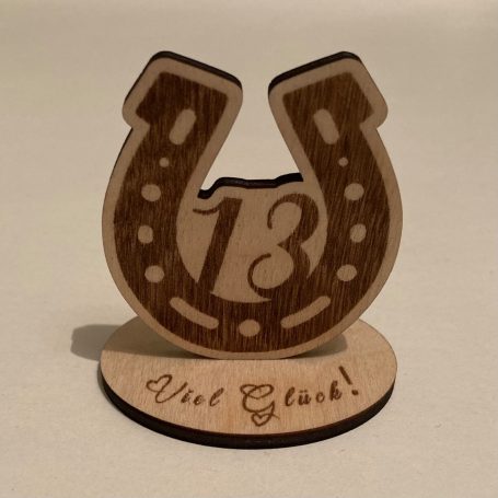 Ein hölzernes Hufeisen mit der Zahl 13 und der Aufschrift „Viel Glück!“.