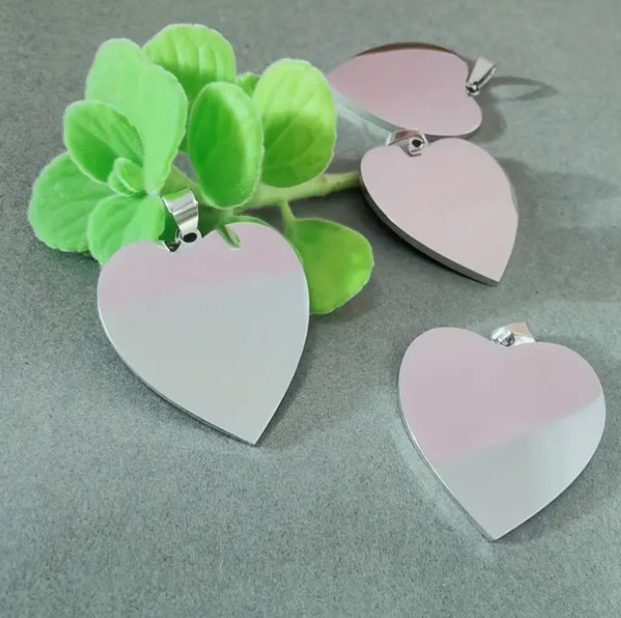 Vier herzförmige, silberne Anhänger neben einem grünen Pflänzchen.