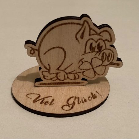 Ein hölzernes Schweinchen mit einer Blume und dem Schriftzug "Viel Glück!".