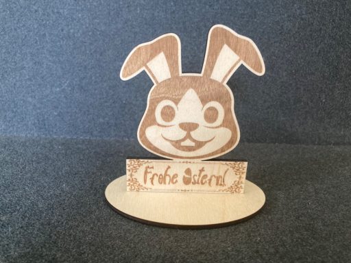 Süßer Hase aus Holz mit dem Schriftzug „Frohe Ostern“ in dekorativer Schrift.