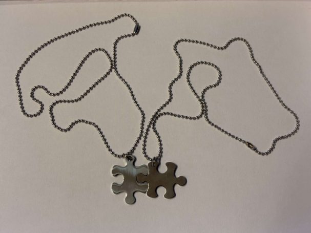 Ein silbernes Puzzlestück hängt an einer Kette auf einem hellen Hintergrund.