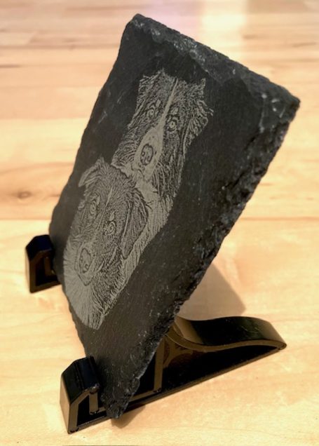 Schieferplatte mit graviertem Hundemotiv und schwarzem Ständer.