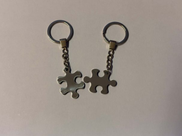Zwei Schlüsselanhänger in Form von Puzzlestücken, verbunden durch eine Kette.