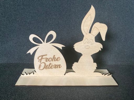 Osterhase sitzt neben einem Osterei mit der Aufschrift „Frohe Ostern“.