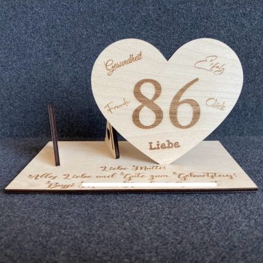 Holzherz mit der Aufschrift "86" und personalisiertem Text auf einer Holz Unterlage.