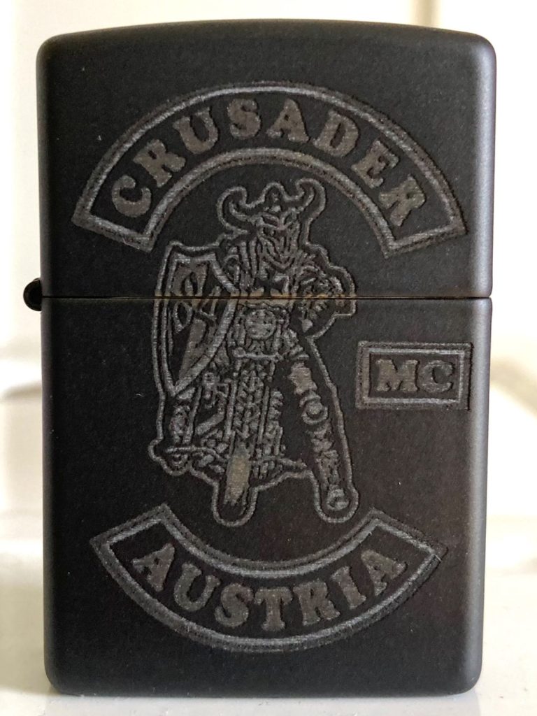 Schwarze Zippo-Feuerzeug mit eingraviertem "CRUSADER MC Austria"-Logo.