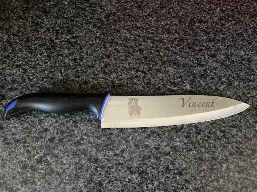 Kochmesser mit schwarzem Griff und gravierter Klinge auf einer dunklen Oberfläche.