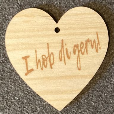 Herzförmiges Holzschild mit der Aufschrift "I hob di gern!" in heller Schrift.
