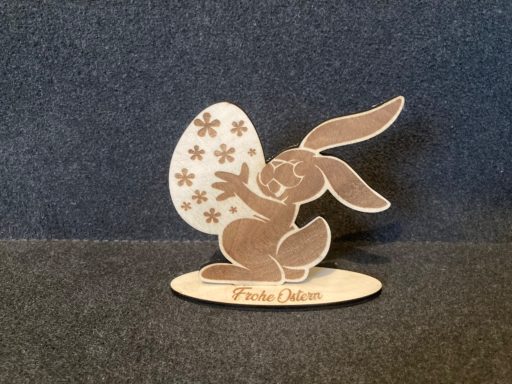 Holzfigur eines Hasen, der ein buntes Osterei mit Mustern hält.